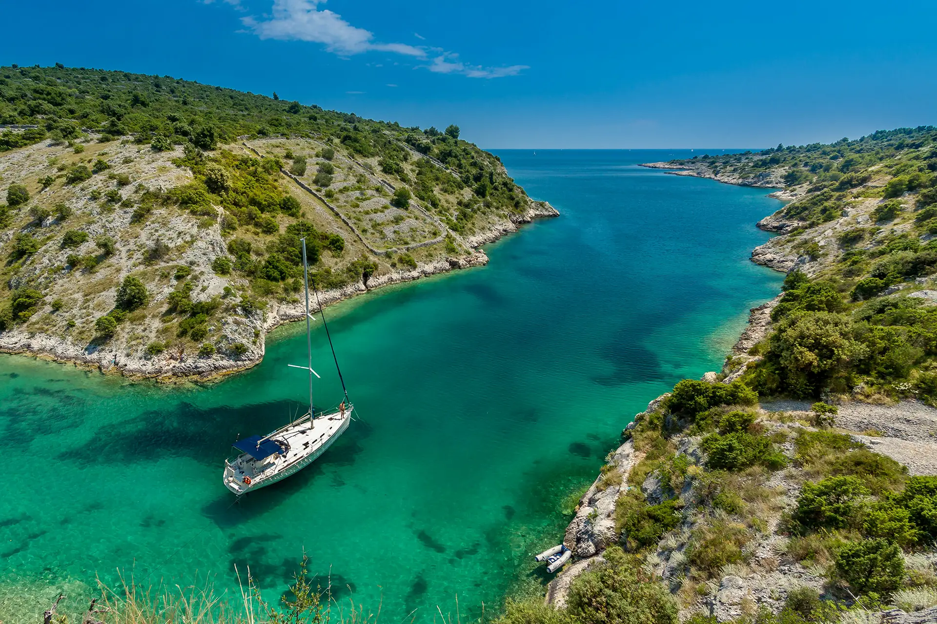 Aerial view of a sailboat anchored in a secluded cove with crystal-clear turquoise water.